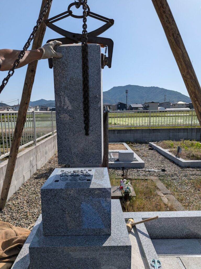 チェーンブロックとクランプを使い、お墓の石を吊り上げて据え付けている作業風景