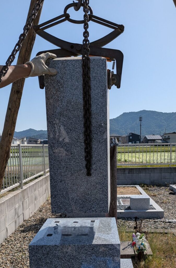 クランプで墓石を挟んで吊り上げている作業風景